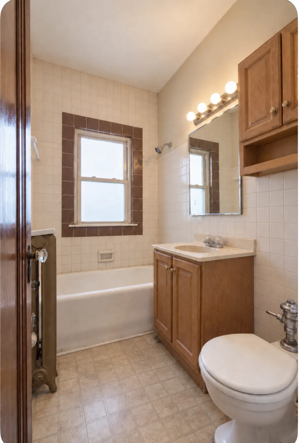 The bathroom before work: oak vanity, wood-framed mirror, beige wall tile and sheet vinyl floor