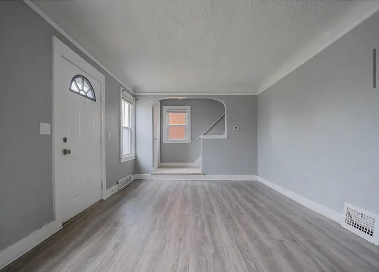 Living room looking toward the front door, with grey walls, new flooring and an arched opening to the stair